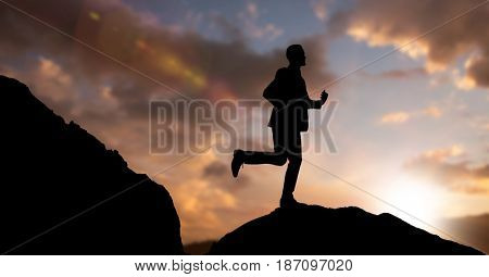 Digital composite of Silhouette businessman running on mountain against sky during dusk