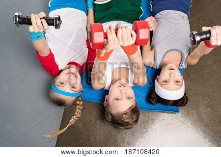 Top View Of Cute Children In Sportswear Lying On Yoga Mat And Exercising With Dumbbells In Gym, Chil
