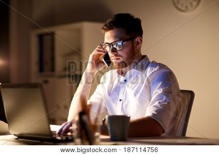 business, overwork, people, deadline and technology concept - businessman in glasses with laptop computer calling on smartphone at night office