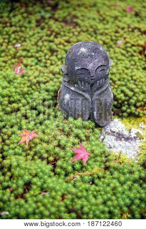 Stone Statue Of Jizo On Ground Covered By Green Star Moss And Red Maple Leaves During Autumn In A Ga
