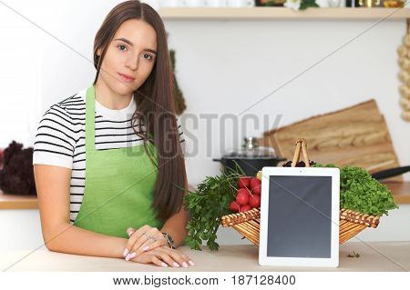 Young woman is making online shopping by tablet computer and credit card. Housewife found new recipe for cooking in a kitchen.