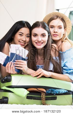 Three Young Smiling Women Holding Passports And Tickets While Packing Suitcase, Getting Ready To Tra