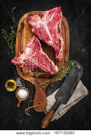 Raw dry aged t-bone steaks for grill with fresh herbs and cleaver