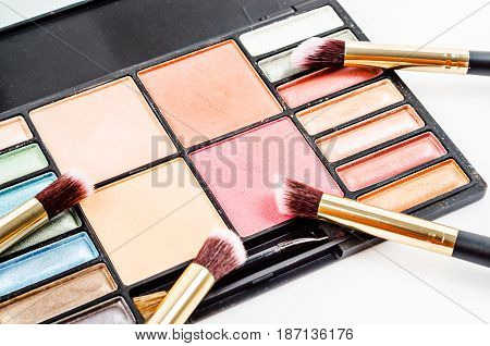 Crushed blush and eyeshadow makeup in set palette with brush on white background.