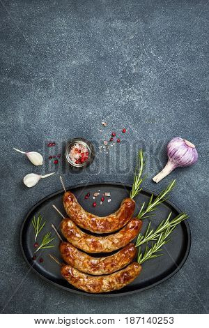 Grilled homemade rosemary sausages skewers on iron frying pan over rustic dark stone kitchen table. Top view flat lay