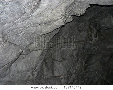 Cave entrance - rocky wall out into the darkness. Gray stone texture with cracks and roughness.