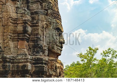 Smiling stone face of Prasat Bayon the central temple of Angkor Thom Complex, Siem Reap, Cambodia. Ancient Khmer temple is surrounded by tropical trees famous Cambodian landmark, World Heritage.