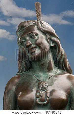 Napier New Zealand - March 9 2017: Closeup of the face of the iconic Maori symbol Pania of the Reef. Bronze statue in the beach park against blue sky with a few white clouds.