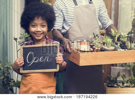 Man Carrying Plants Standing With Son Showing Open Sign