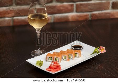 Philadelphia maki sushi rolls with salmon cheese cream cucumber on white plate and glass of wine
