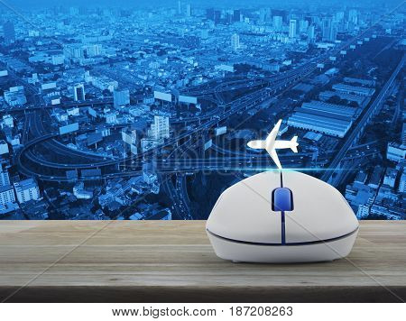 Airplane icon with wireless computer mouse on wooden table over city tower street and expressway Business transportation concept