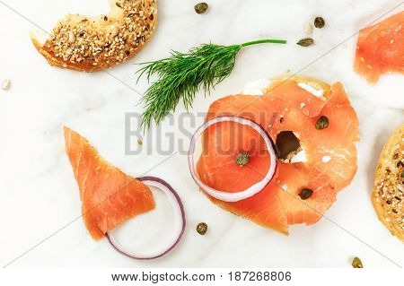 Bagel ingredients. Lox, purple onions, capers, dill, and the buns, shot from above on a white marble background in the process of making, with a place for text
