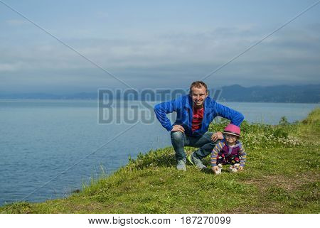 Dad and daughter are amusing and funny sitting on the edge of the beach by the sea