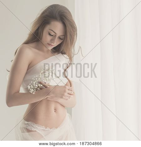 Sensual girl with flowers by the window. She's wearing white underwear.