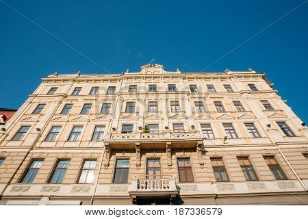 Riga, Latvia. Bottom View Of Main Facade Of Old Building In Classical Style, Decorated By Pilasters, Pediment And Balcony On Jekaba Street In Old Town In Sunny Day Under Blue Clear Sky.