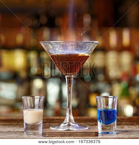 A spectacular cocktail with fire on the blurred background of the bar in the nightclub. In a cocktail pour a burning sambuca. Space for text design