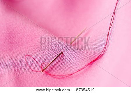 needlework and tailoring concept - sewing needle with thread stuck into pink fabric