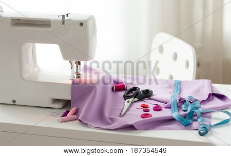 needlework, technology and tailoring concept - sewing machine with scissors, buttons, tape measure and fabric