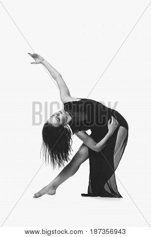 Beautiful modern dancer young woman in black flyings fabrics making dance moves. Isolated on white background. Copy space. Monochrome.