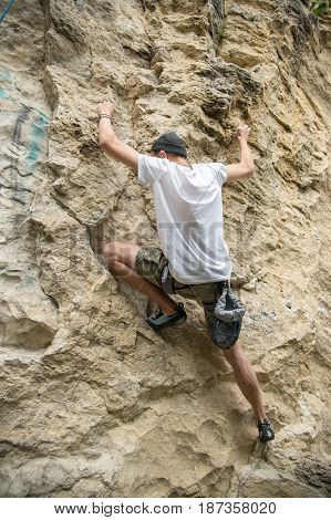 The lean guy in the hat of shorts and a T-shirt is engaged in rock climbing on a steep rock without insurance