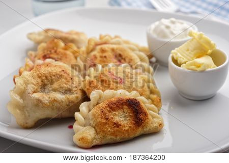Traditional Polish dumplings Pierogi ruskie with sour cream and butter on a rustic table