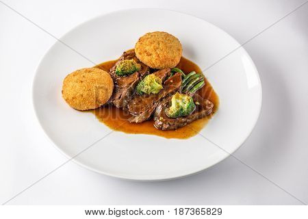 Beef cheeks in sauce with broccoli and green beans on a white plate. Selective focus. Isolated on white background