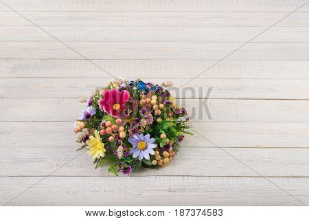Colorful composition made of artificial flowers, fruits, butterflies, birds and ears of wheat in stylish vase on white woden background.
