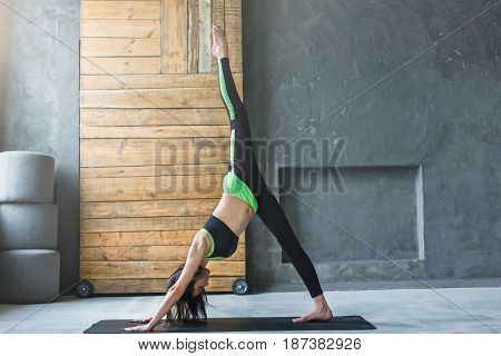 Young woman in yoga class making One-Legged Downward-Facing Dog Pose. Healthy lifestyle in fitness club. Stretching