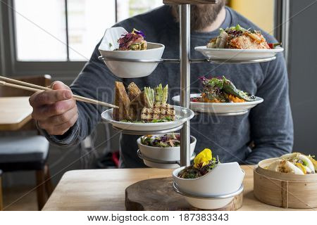 Man Picking Tofu From Tiered Server Using Chopsticks