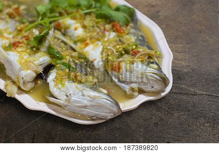 Steamed sea bass with lemon chili and garlic sauce in bowl on old relic wooden table. selective focus with clipping path.