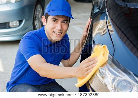 Young man polishing (cleaning) car with microfiber cloth - car detailing valeting and auto service concepts