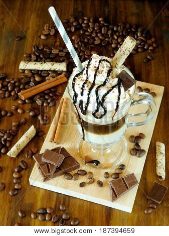 Coffee cocktail with whipped cream in an Irish coffee mug surrounded by coffee beans, cinnamon and chocolate bars