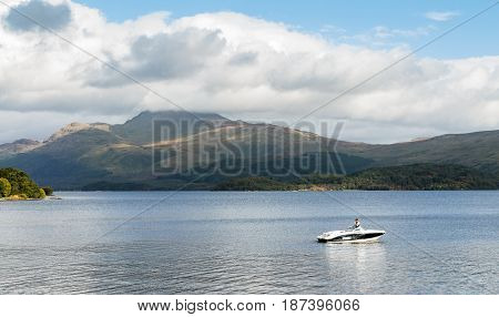 LOSS ARGYLL SCOTLAND - SEPTEMBER 27 2014: stationary speedboat with man on board floating on the calm waters of Loch Lomond with Ben Lomond mountain in the background on a sunny and bright day.