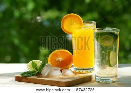 A glass of orange and lime juice on a wooden board with ice cubes and mint