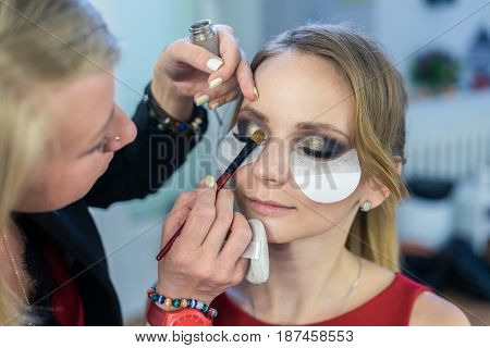 Make-up artist doing smoky eyes makeup to beautiful young girl in the studio Dressing room