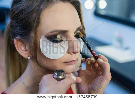 Make-up artist doing smoky eyes makeup to beautiful young girl in the studio Dressing room