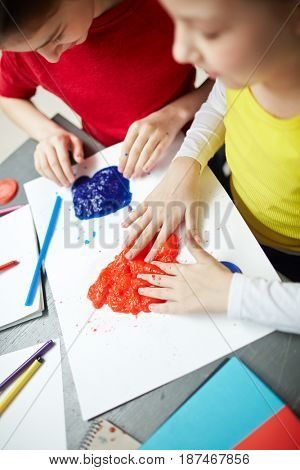 High angle portrait of two little girls plying with playdough during art class, enjoying feeling it with fingers, developing fine motor skills