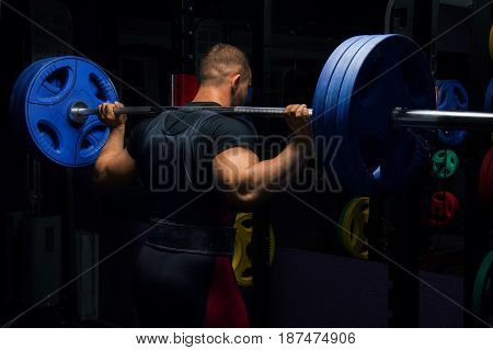 Professional athlete stands in the gym with a barbell on his shoulders