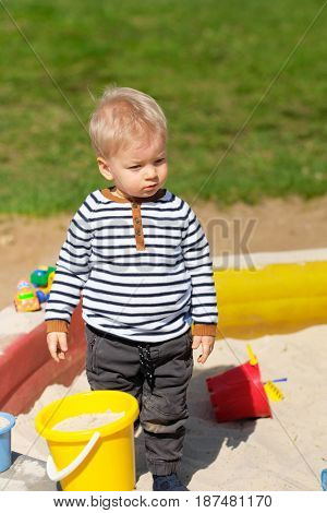 Portrait of toddler child outdoors. One year old baby boy playing with sand at playground sandbox