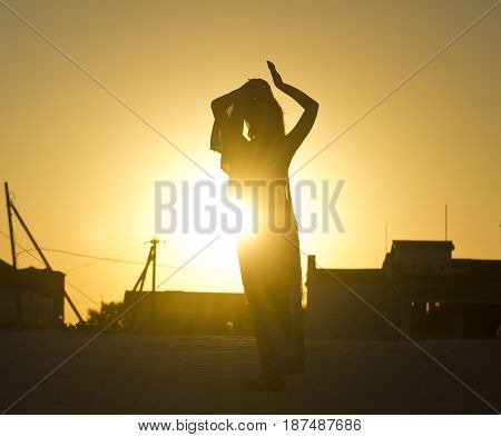 silhouette of girl against the yellow sun rays at sunset with buildings on gackground