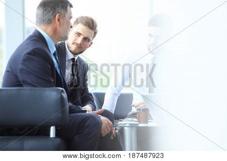Mature businessman using a digital tablet to discuss information with a younger colleague in a modern business lounge