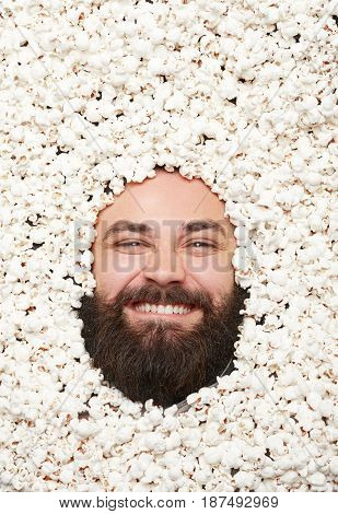 Male bearded face lying on popcorn looking at camera excitedly.