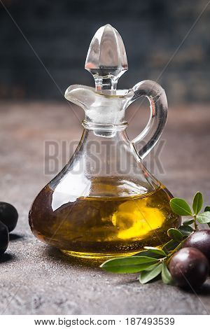 Olive oil in a glass bottle and olive branch on brown stone table