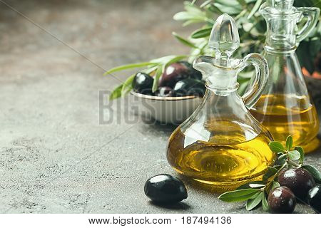 Olive oil in a glass bottle and olive branch on brown stone table