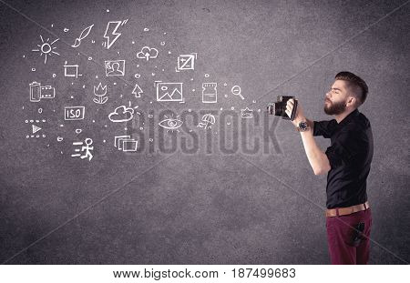 An elegant hipster guy trying to use a vintage camera with camera settings icons drawn on wall, like flash, white balace or ISO value concept