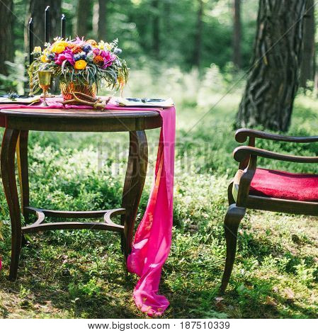 Decorated Wooden Table Served For Two In The Garden On Grass On The Riverbank. Boho And Rustic Style