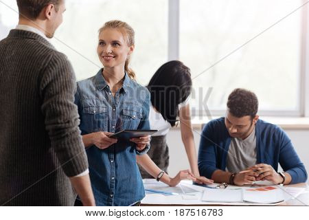 Discussing work. Joyful positive nice woman holding a tablet and discussing work issues while talking to her colleague