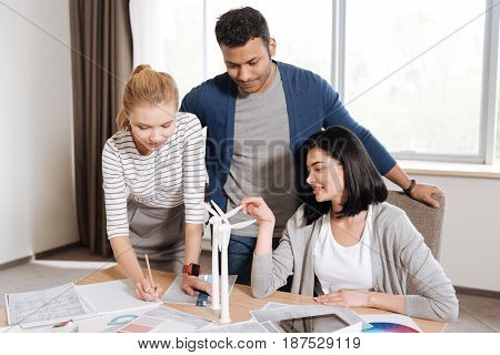 Working with colleagues. Good looking serious blonde woman leaning on the table and making some notes while working with her colleagues