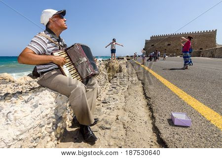 HERAKLION GREECE - JULY 16 2016: Crete. Musician on the waterfront plays accordion. In the background Venetian fortress.