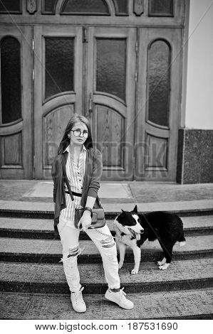 Trendy Girl At Glasses And Ripped Jeans With Russo-european Laika (husky) Dog On A Leash, Against Wo